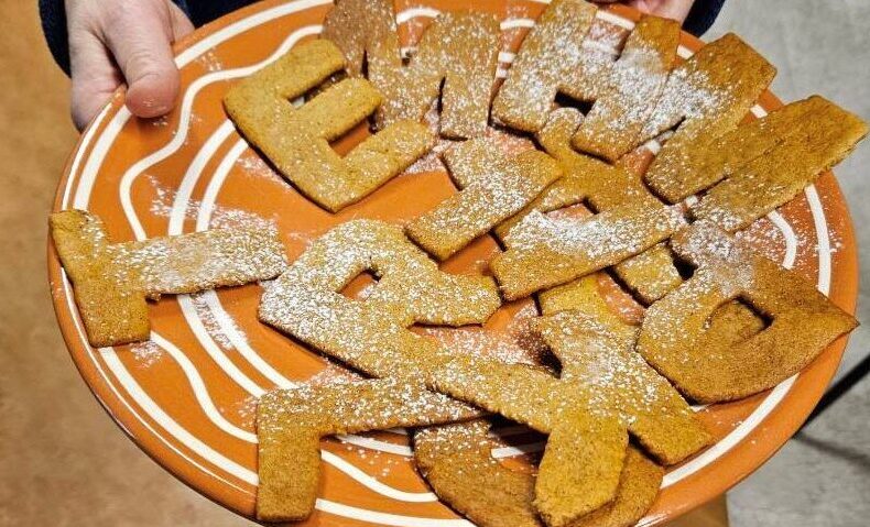 pepparkakor formade som bokstäver ligger på ett stort fat i rödbrun färg med vit bård.